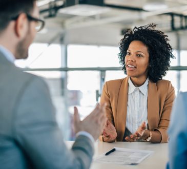 Black woman in job interview sitting across table from interviewers.
