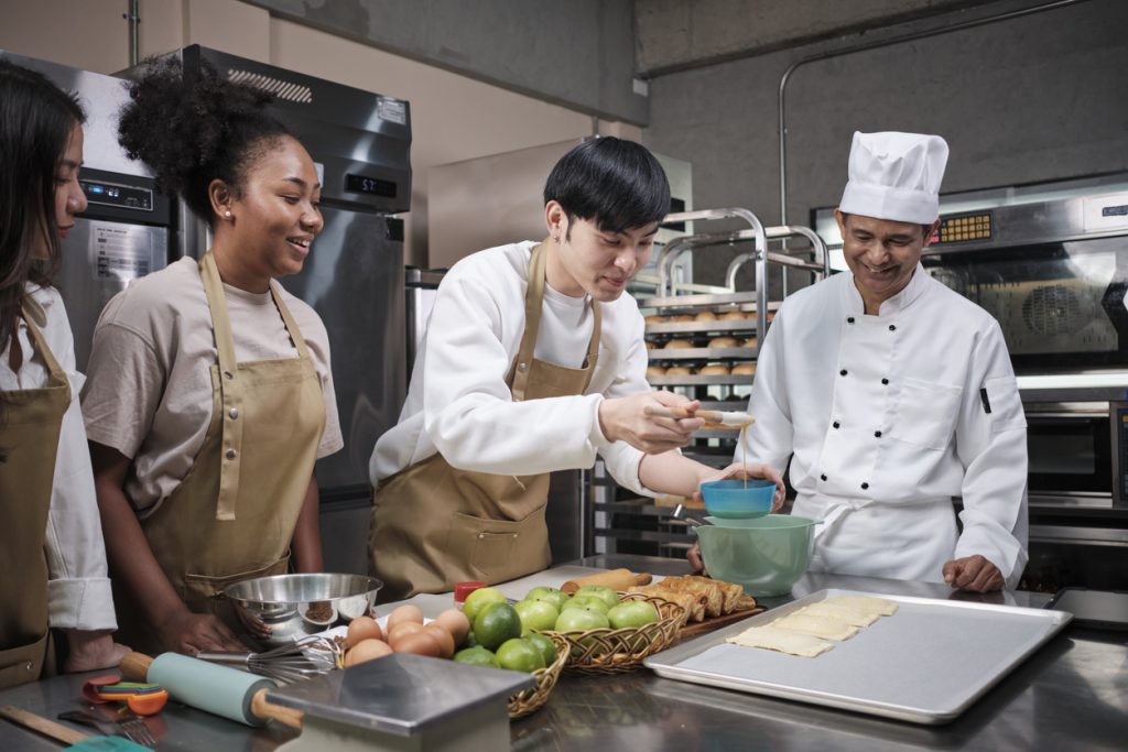 Students learning how to cook from chef in kitchen.