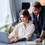 One person standing behind another working on laptop