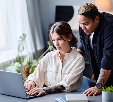 One person standing behind another working on laptop