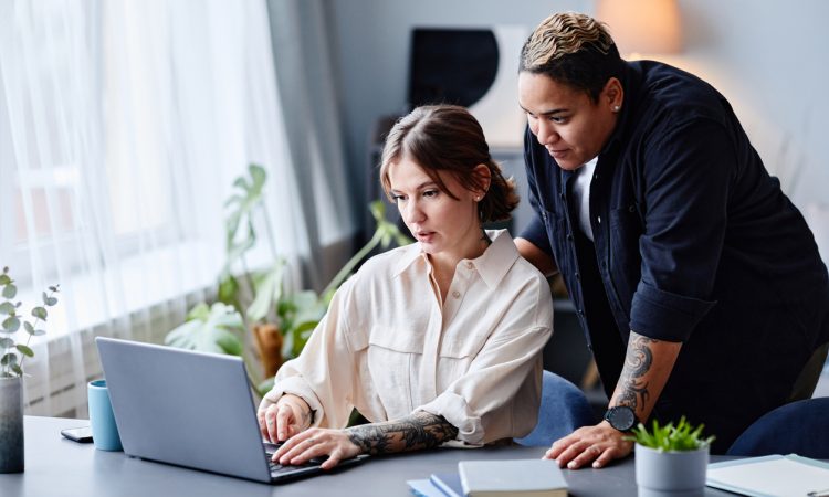 One person standing behind another working on laptop