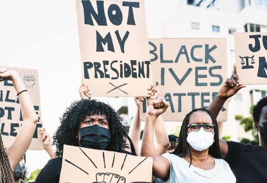 Black Lives Matter protest during the pandemic, with people holding signs reading "not my president" and "black lives matter."