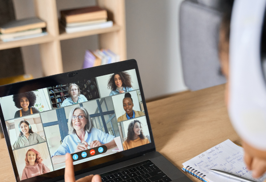 Student wearing headphones and watching live online class with professor and other students on the screen.