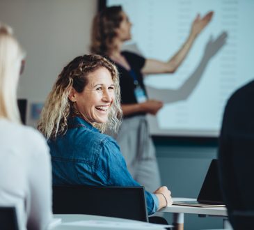 Rear view of a woman sitting in audience looking back at a colleague and smiling during a conference.