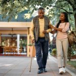 Young woman supporting arm of older man walking with cane