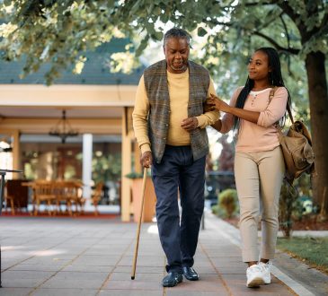 Young woman supporting arm of older man walking with cane