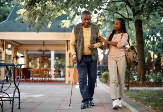 Young woman supporting arm of older man walking with cane