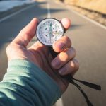 Close-up of hand holding compass against backdrop of mountain road