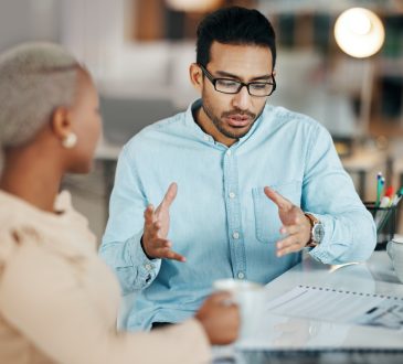 Two people sitting and talking at desk.