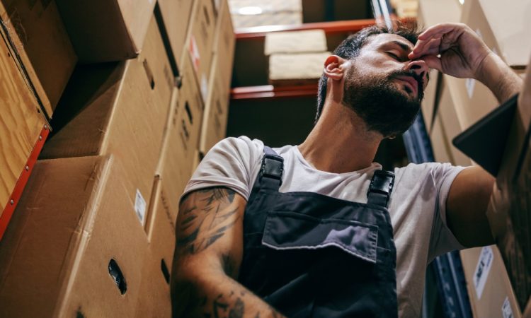 Stressed man at work, crouching down between boxes in back room