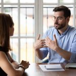Two people sitting at table in office talking