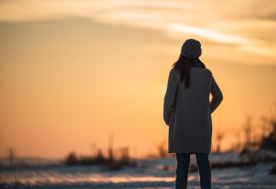 Woman pictured from behind standing outside looking at snowy landscape at dusk