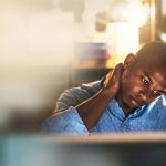 Man sitting at computer in office rubbing neck