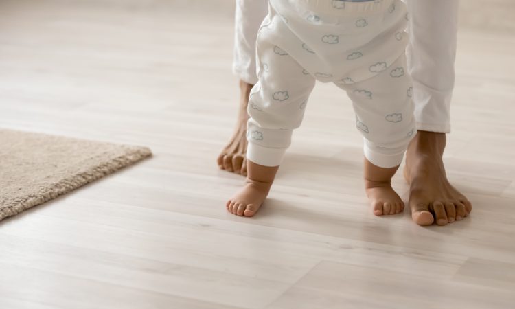 Photo of toddler trying to walk with mom behind, seen from waist down
