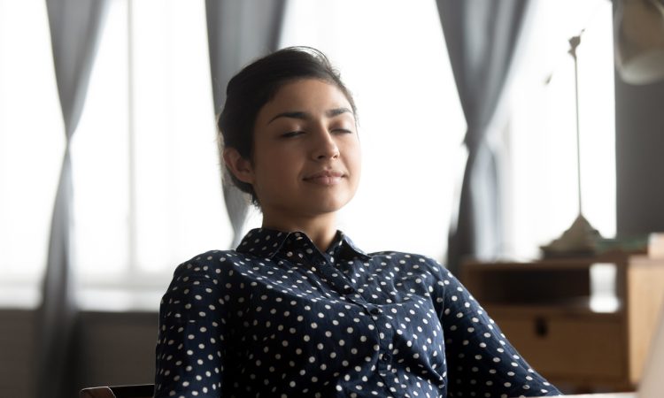 Woman sits at desk with eyes closed
