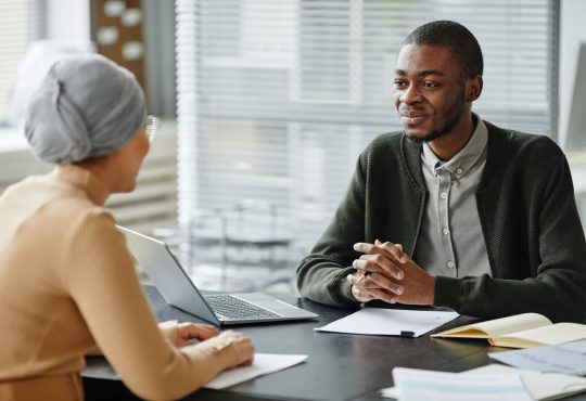 Two people sitting across desk from each other in job interview in office