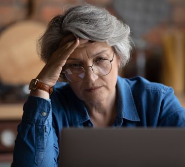 Older woman looking at laptop with their hand on their forehead.