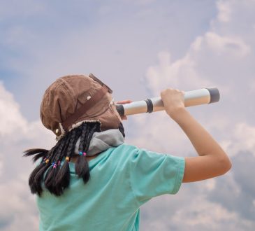 A child looking up at the cloudy sky through a spyglass.