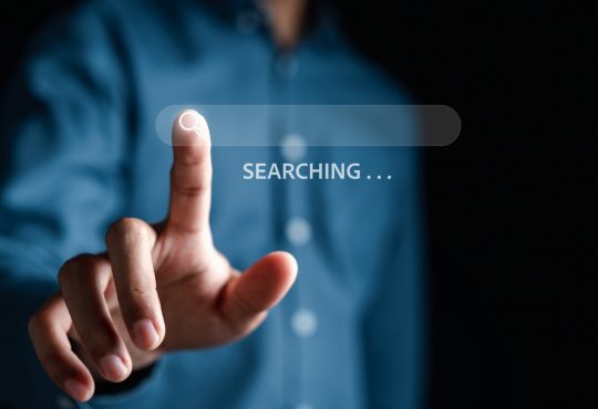 The image shows a person pressing a virtual search icon on a transparent search bar, with the word "SEARCHING..." displayed.