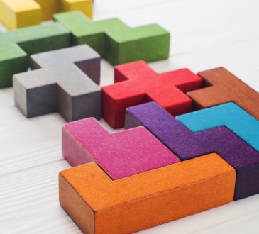 The image shows colorful 3D puzzle pieces resembling Tetris blocks arranged on a white surface.
