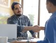 Two people shaking hands across desk in office