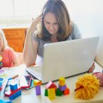 Stressed mom trying to work on computer at home beside screaming child