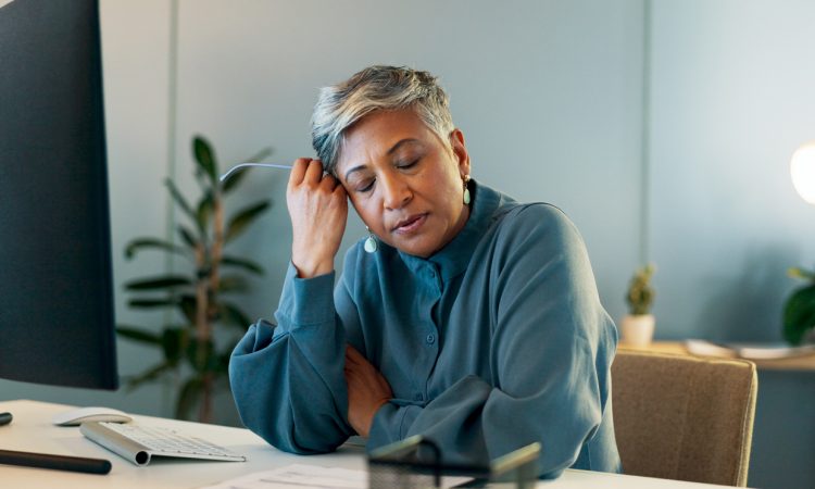 Stressed woman in office resting head on hand with eyes closed