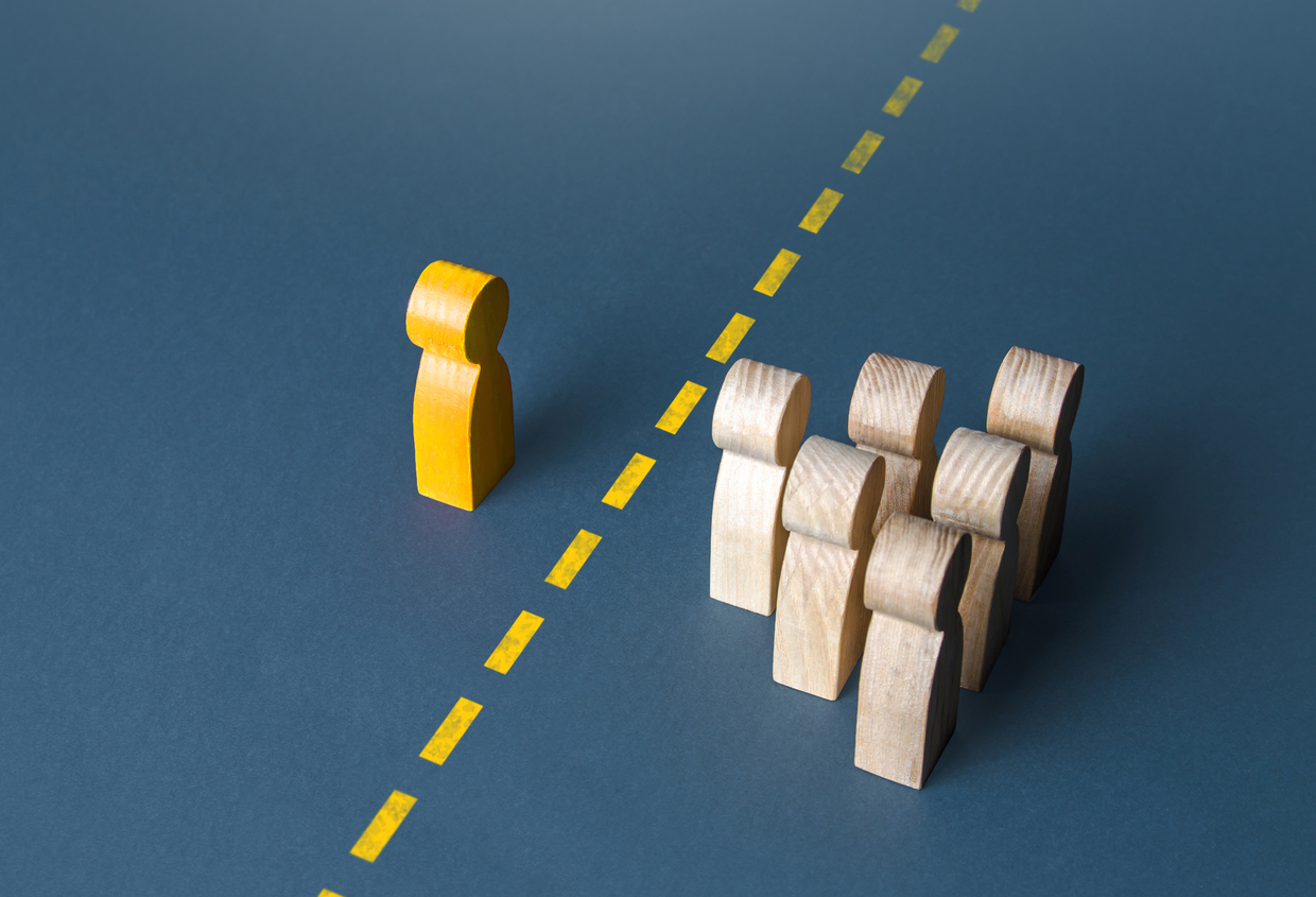 Wooden figurines of a person and a group of people are separated by a yellow line.