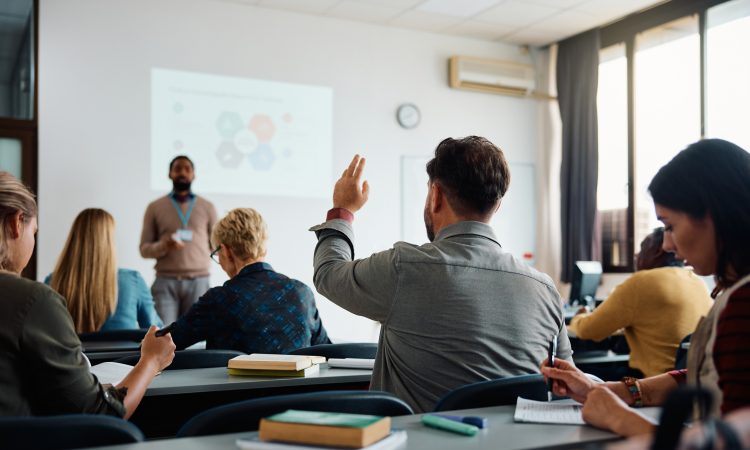 Rear view of man raising arm to ask a question during a presentation in lecture hall.