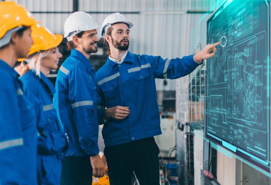 Team of engineers wearing hard hats looking at digital whiteboard together