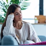 Shot of depressed young woman thinking about her problems while sitting on the sofa at home.