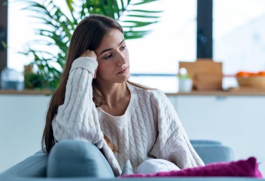 Shot of depressed young woman thinking about her problems while sitting on the sofa at home.