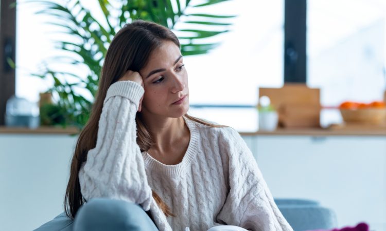 Shot of depressed young woman thinking about her problems while sitting on the sofa at home.