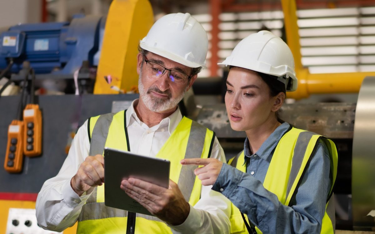 Senior manager on job training technician working in metal sheet production factory.