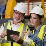 Senior manager on job training technician working in metal sheet production factory.