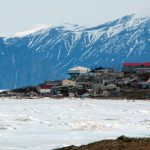 n Photo of Pond Inlet in mid June of 2005 from Salmon Creek, 3.5 kms West of the Hamlet. The mountains are 25kms away and the iceberg is 9kms from town. The community's library (large white roof) and Health Center (large red roof) are the most predominent structures in the photo.