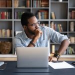 Man sitting at laptop thinking with hand on chin