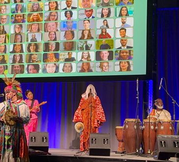 An image of the cultural celebration at Cannexus26 with indigenous music performers holding instruments on a stage. Behind them is a blue curtain and a slide showing photos of CERIC board and staff headshots.