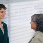 European Caucasian young adult gen z diverse business woman lady standing talk workday task indoor job office place. Teen female worker boss manager make conversation give advice helping consulting discuss client insurance benefit